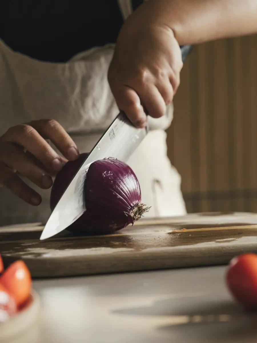 A cook slicing a red onion with a chef’s knife