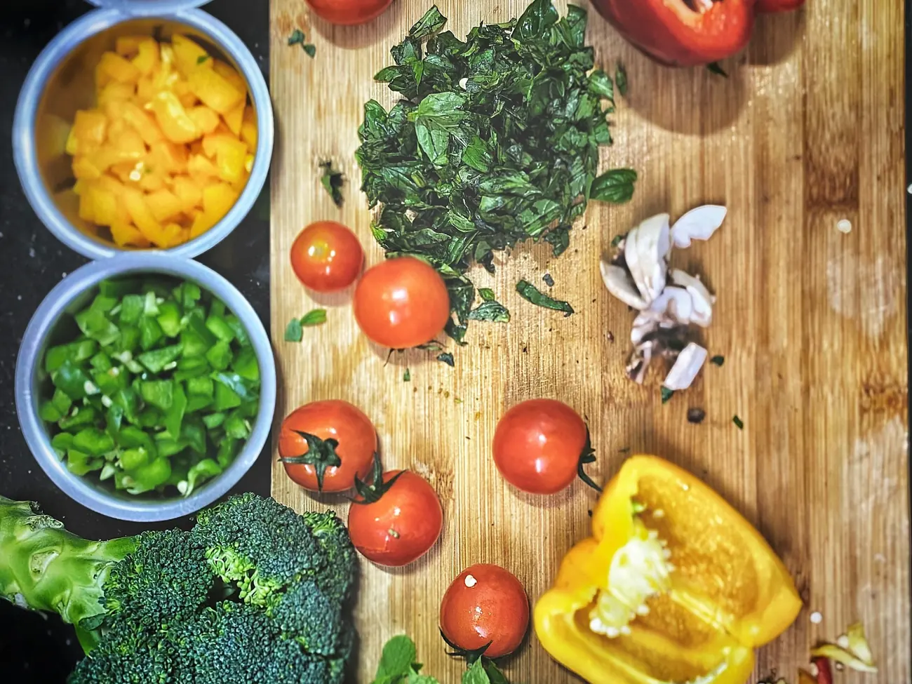 Chopped tomatoes, peppers and broccoli on a wooden board beside bowls of prepped vegetables