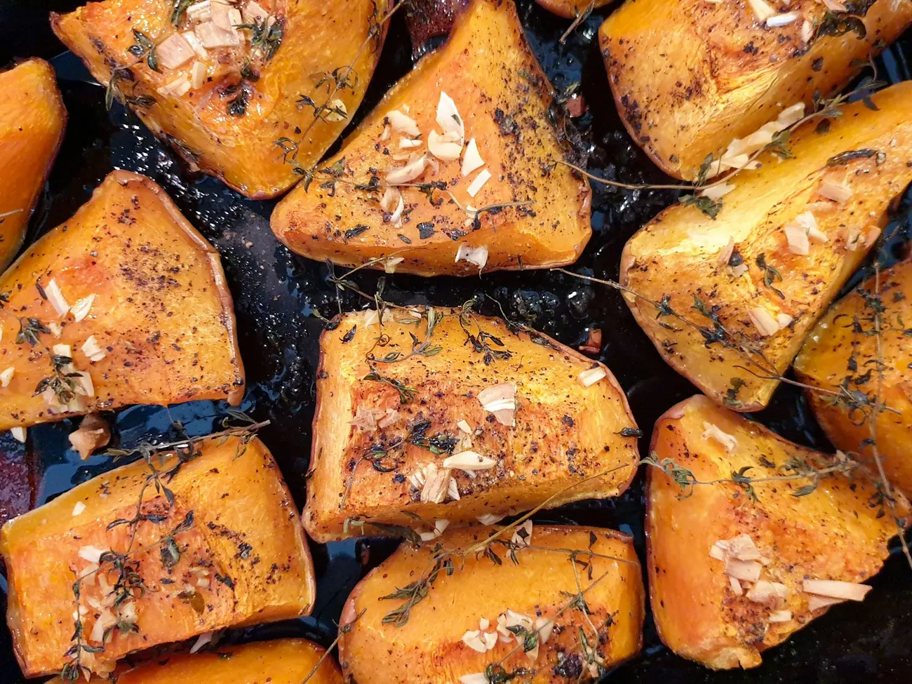 Roasted squash wedges with herbs on a dark sheet pan
