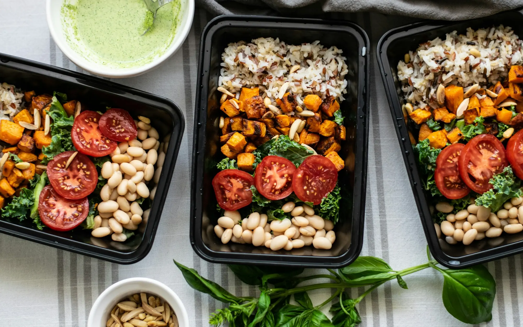 Three meal prep containers with roasted sweet potato, white beans, tomatoes and kale, made in a Pan & Plates session
